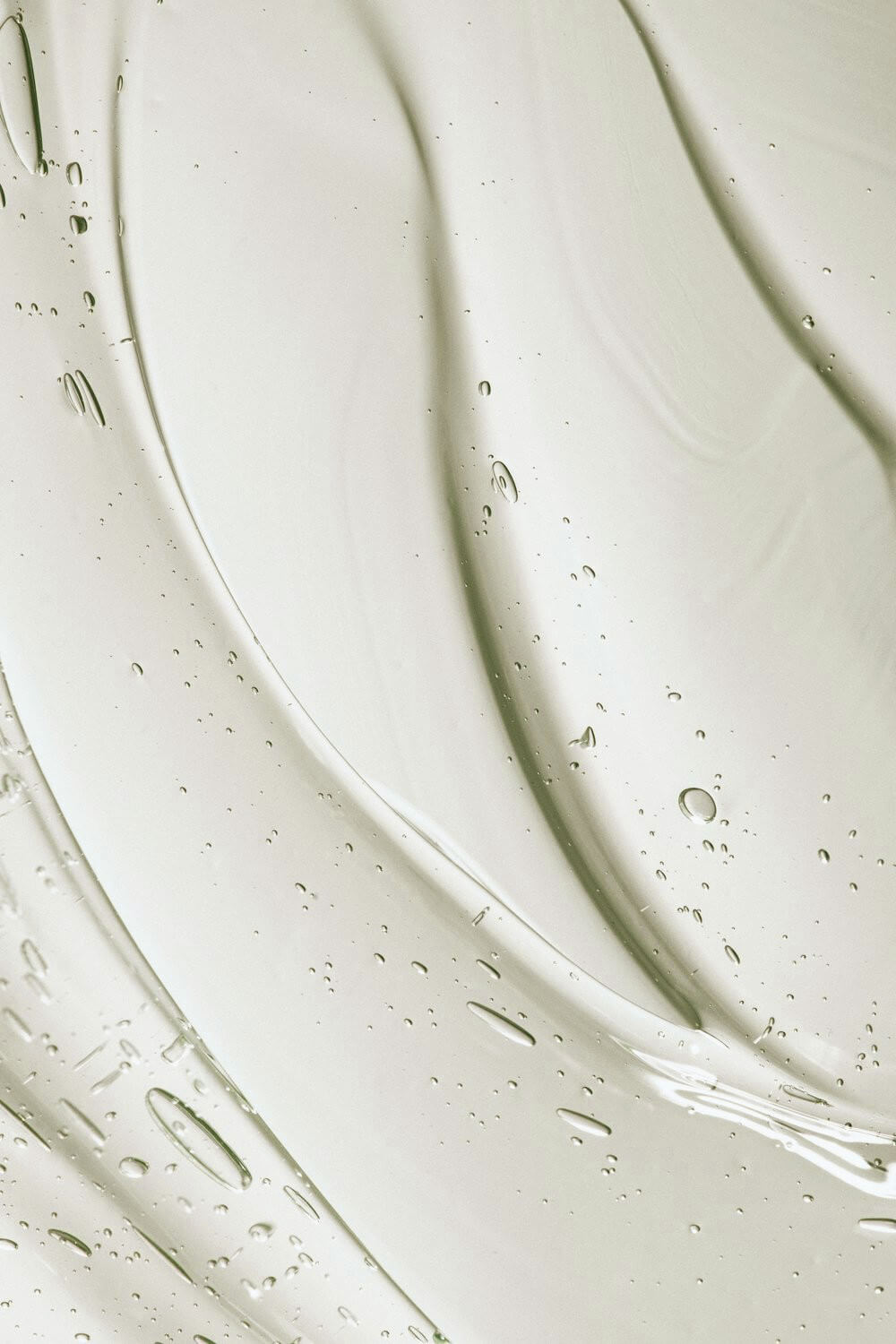 Nahaufnahme eines durchscheinenden Gels mit kleinen Bläschen und glatten, gewellten Streifen vor einem hellen Hintergrund, der ein abstraktes Muster hervorhebt - perfekt, um die beruhigenden Eigenschaften der Hestakofi Augencreme zu präsentieren.