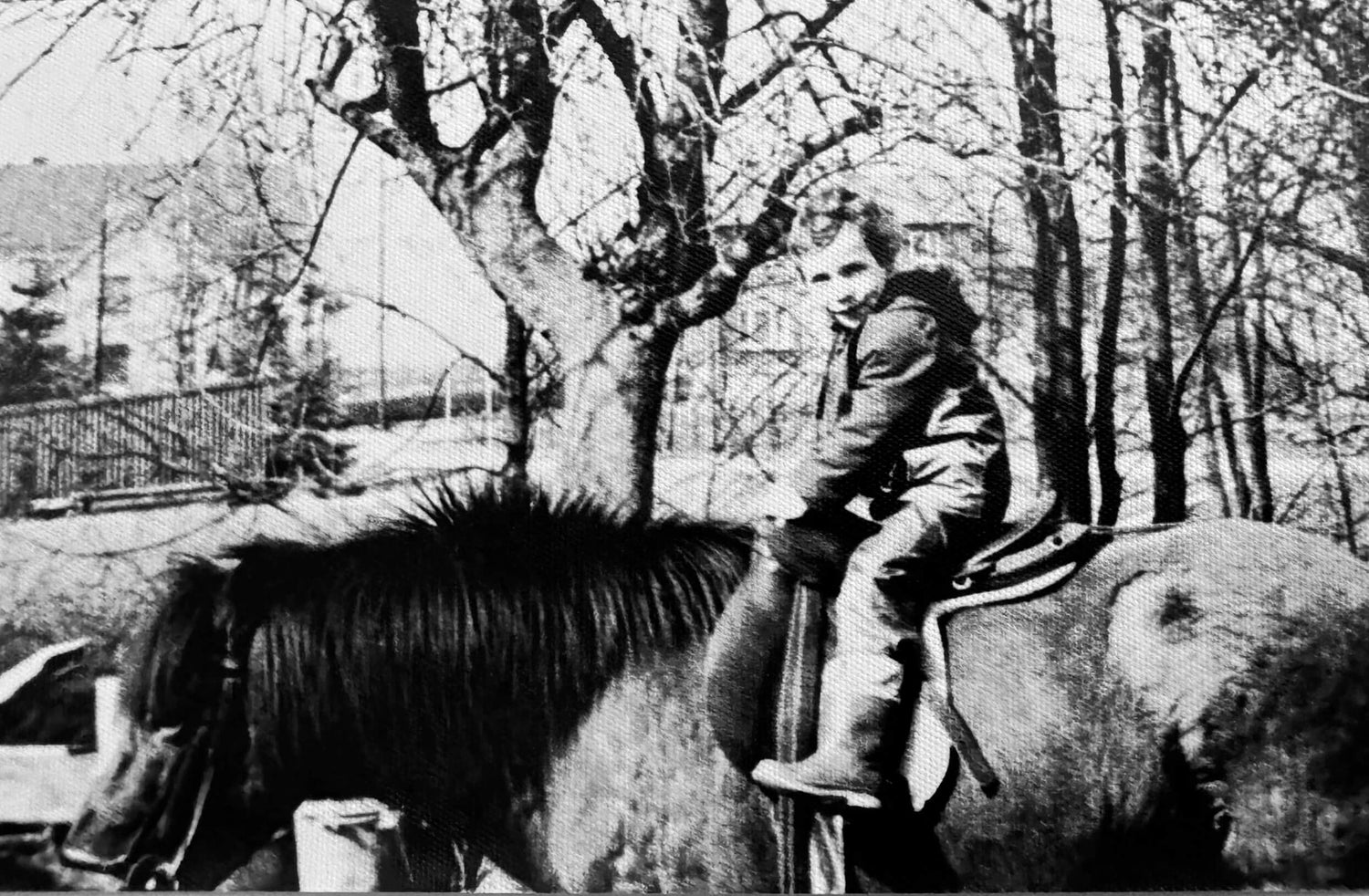 Ein Schwarz-Weiß-Foto eines kleinen Kindes in Winterkleidung, das auf einem Pferd im Freien sitzt, mit kahlen Bäumen und Gebäuden im Hintergrund.