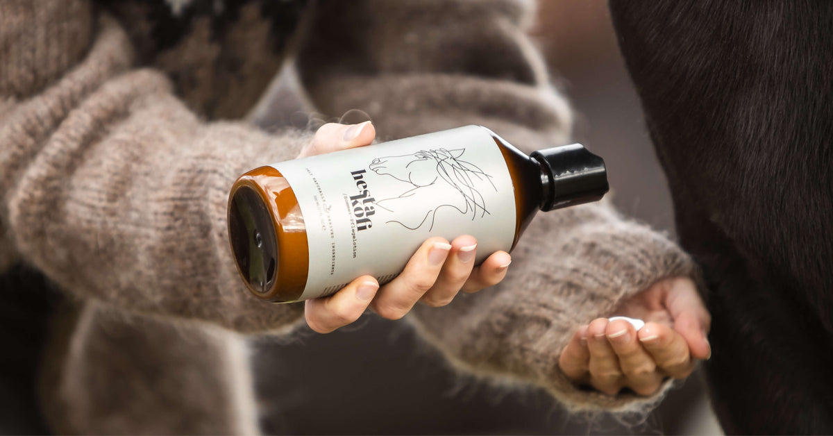 Braune Flasche mit Hestakofi logo. Eine Frauen Hand im Islandpullver hält etwas Lotion in der Hand